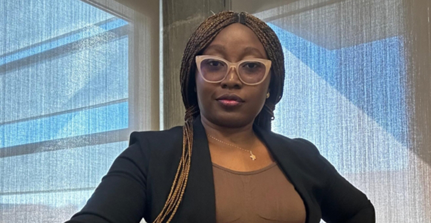 Black female with dark hair wearing glasses and a black suit and brown shirt